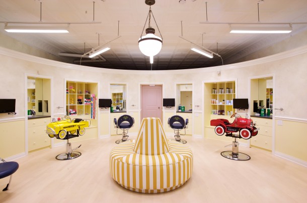 main view of children's hair salon, Circa lighting schoolhouse light fixture with Perennials fabric of yellow and white striped covering a bourne seat. kid's cutting stations featuring a red firetruck and yellow taxi seats