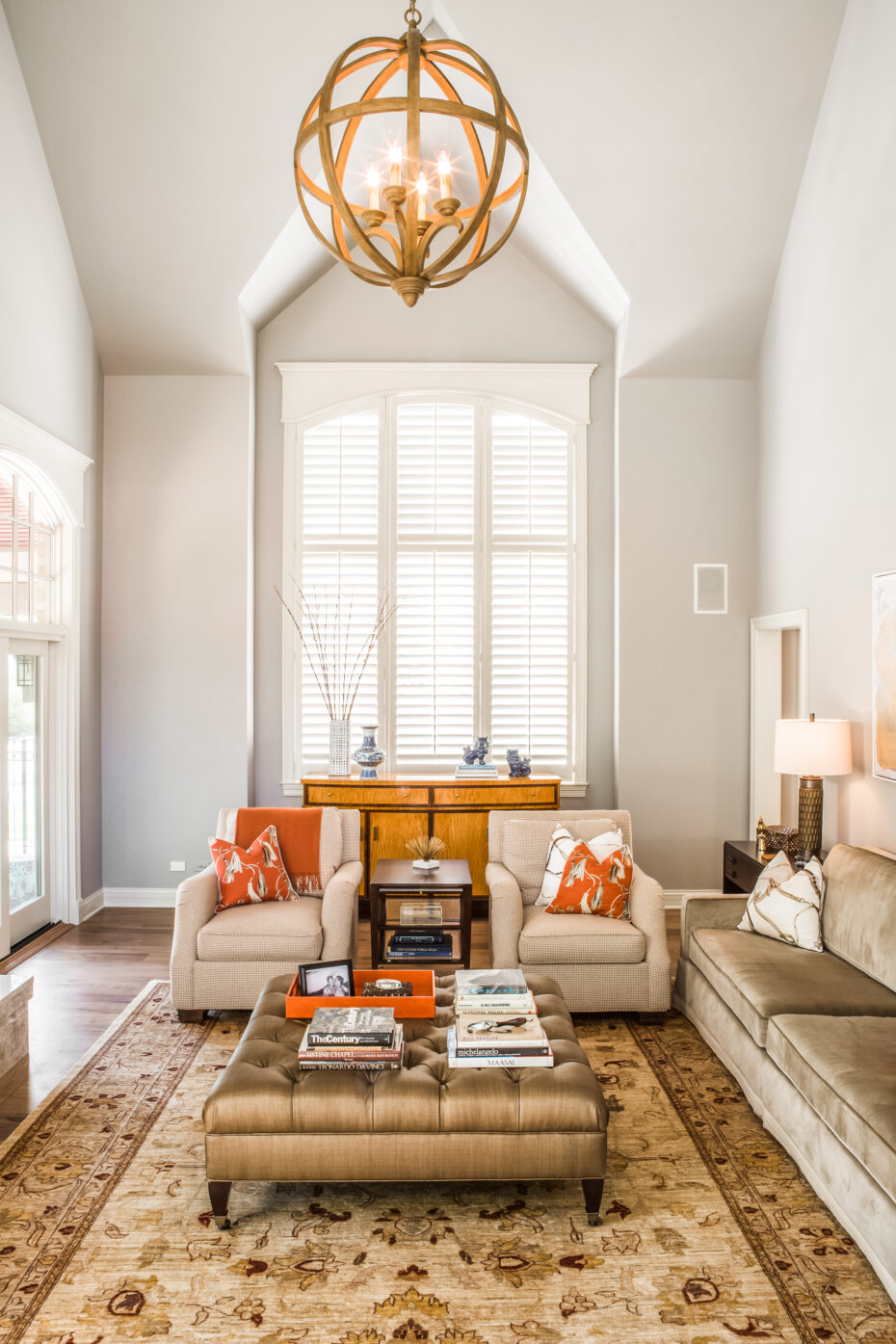 living room with volume ceilings, curry and co light fixture, neutral color with orange accents