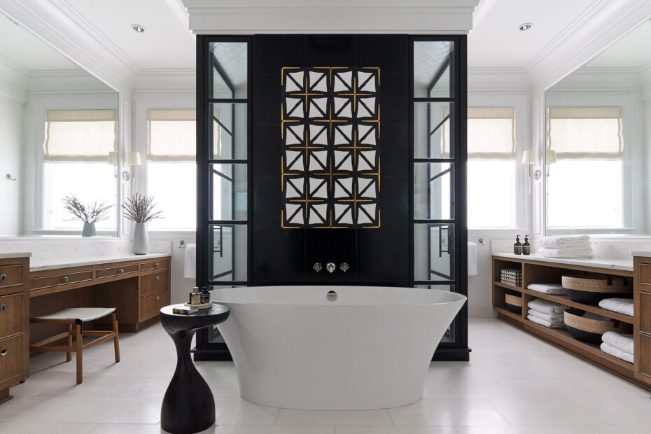 Large bathroom with black, white and brass mosaic tile. White Soaking Tub. Wood cabinets. White Stone floor.