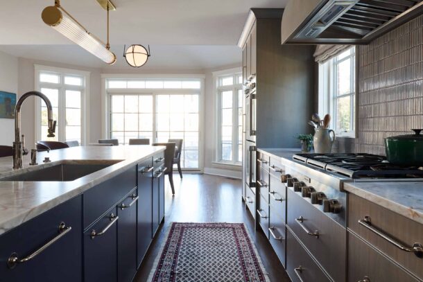 this image if of a kitchen with a dark blue island with light quartz countertops, light grey cabinets, looking into a breakfast room